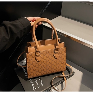 Macro detail of brown square crossbody bag with M-letter pattern on design books