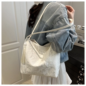 Detailed close-up of white lace shoulder bag with butterfly embroidery and tassel decor