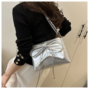 Détail du sac à bandoulière argenté avec nœud et chaîne sur un pull noir ajusté