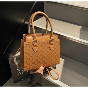 Detail of a brown square tote bag with repeat M pattern and gold metal ring connectors