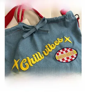 Detail of blue denim bucket bag with yellow Chill vibes embroidery and red textile strap