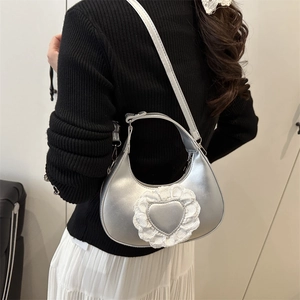 Silver crescent moon shoulder bag with heart lace detail worn by a model in a minimal setting