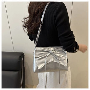 Détail d'un sac bandoulière argenté métallisé avec grand nœud et chaîne sur un mannequin