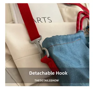 Detail of light blue denim bag featuring a red fabric strap and a detachable grey hook