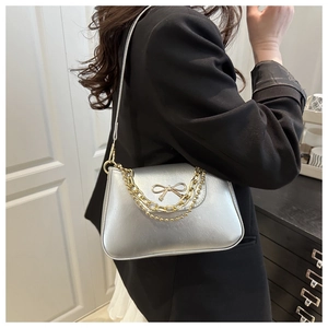 Detailed view of silver shoulder bag featuring a golden bow buckle and chain strap detail