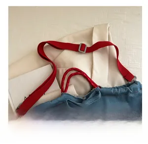 Detail of blue denim crossbody bag featuring yellow embroidery and red fabric shoulder strap