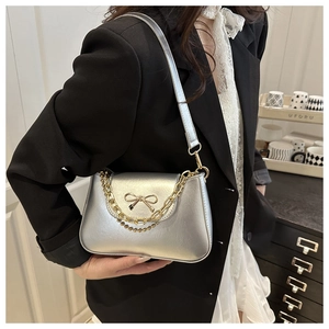 Detail of silver matte shoulder bag with golden bow accent and chain straps on model