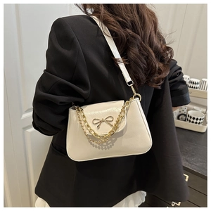 Detail of cream shoulder bag with gold bow clasp and chain strap worn on dark blazer