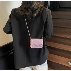 Detail of a shiny pink crocodile texture crossbody bag with silver chain strap on a model