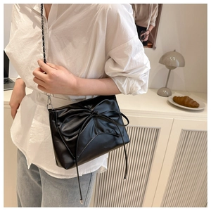 Détail du sac bandoulière noir avec grand nœud et bandoulière en chaîne cuir