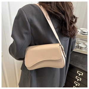 Minimalist beige shoulder bag with irregular wave flap shown on person with grey blazer