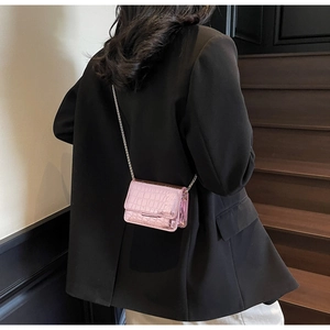 Detail view of mini pink crocodile textured chain bag worn on dark blazer outfit