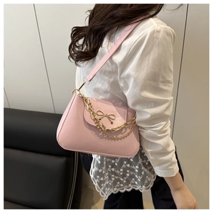 Detail of pink patent leather shoulder bag with metal bow and chain strap on model