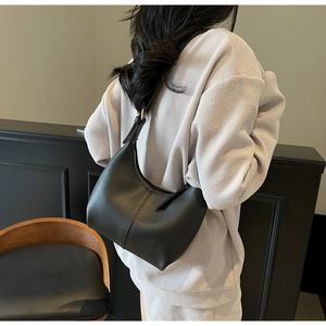 Side view of black matte leather crescent underarm bag worn with casual grey outfit