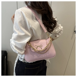 Side view of pink leather underarm bag with gold bow and decorative metal chains