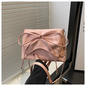 Détail du sac bandoulière rose avec nœud 3D et bandoulière chaîne sur fond clair
