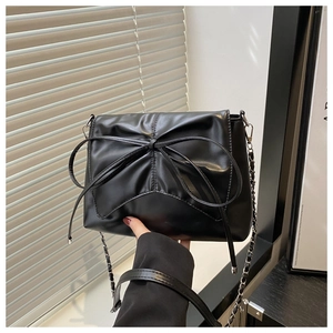Détail d'un sac bandoulière en cuir noir avec un grand nœud et une chaîne argentée