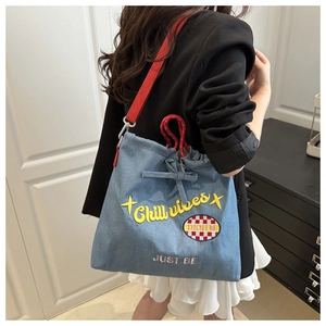 Blue denim tote bag detail featuring Chill Vibes embroidery and red strap on model