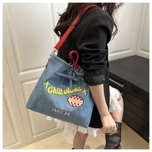 Detail of denim tote bag with yellow 'Chill vibes' embroidery and red straps