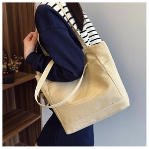 Dettaglio della borsa tote in tela beige con tracolla e tasca laterale su modella