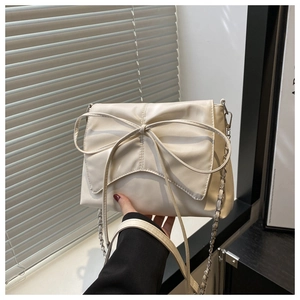 Détail d'un sac crème avec un grand nœud décoratif et une bandoulière en chaîne