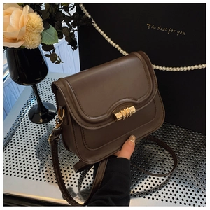 Detail of a brown leather crossbody bag with a unique gold cylindrical metal lock