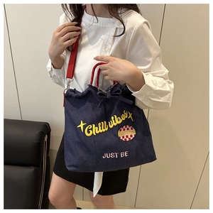Detail of blue denim tote bag with Chill Vibes embroidery and red woven shoulder strap
