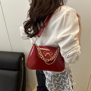 Glossy red faux leather shoulder bag with a gold bow buckle and decorative chains