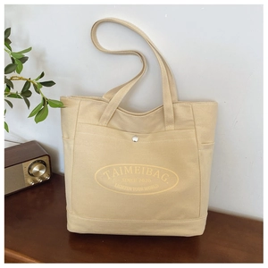 Dettaglio della borsa tote in tela beige con tasca frontale, bottone e logo stampato