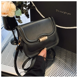 Close-up of black leather crossbody bag with gold cylindrical clasp on gift box