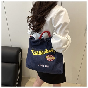 Detailed close-up of blue denim tote bag featuring yellow Chill Vibes 3D embroidery and red straps