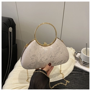 Makroaufnahme der elfenbeinfarbenen Spitze an der Sichltasche mit goldenem Ringgriff