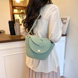 Sac seau tissé vert avec détail perle pour les vacances porté dans un décor de café