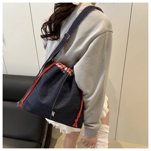 Detailed view of blue denim bucket bag with orange drawstrings and red plaid lining edge