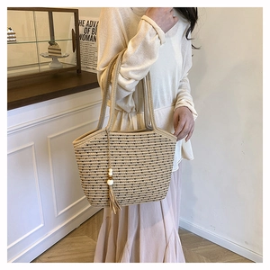 Detail of woven tote bag featuring black dotted patterns and decorative white beaded tassels