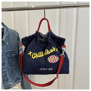 Detail of blue denim drawstring tote with red handles and 'Chill vibes' embroidery