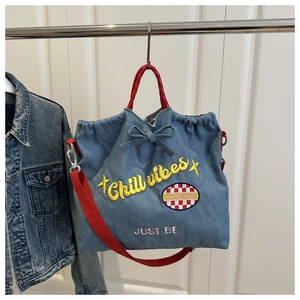 Detail of blue denim tote bag featuring Chill Vibes embroidery and red woven handles