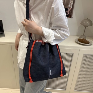 Blue denim bucket bag with orange drawstring rope shown on model in modern setting