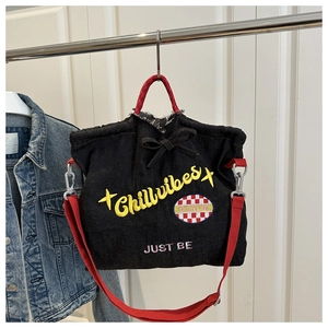 Detail of black denim tote with yellow Chillvibes embroidery and red woven straps