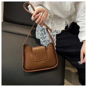 Sac à bandoulière tressé marron porté par un mannequin en chemise de dentelle blanche