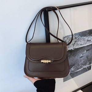 Modern brown leather crossbody bag with a round gold metallic clasp and slim shoulder strap