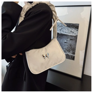Detail of beige underarm bag with silver butterfly charm and pleated bow shoulder strap