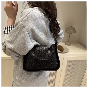 Détail d'un sac à bandoulière tressé noir porté par un mannequin dans un intérieur chic