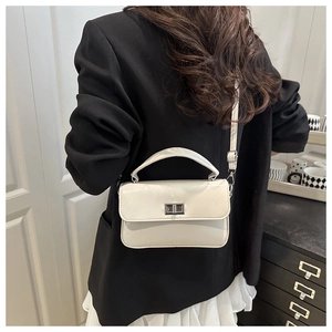 Detail of a chic cream-colored leather handbag with silver turn-lock clasp on a model