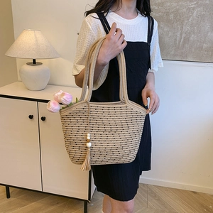 Beige woven tote bag with black dots, long handles, and tassel charm in a lifestyle setting