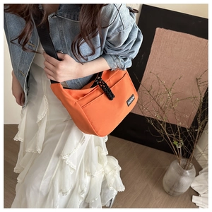 Detail of orange nylon crossbody bag with adjustable strap and fashion label detail