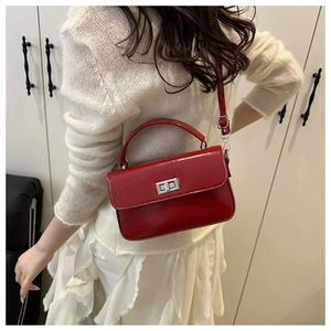 Model wearing a glossy red square leather bag with silver buckle in a minimalist setting