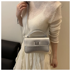 Detail of a silver metallic crossbody bag with dual turn-lock buckle on white knitwear