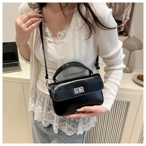 Detail of a black patent leather square bag with silver metal lock and thin strap