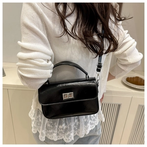 Detail of glossy black crossbody bag featuring a silver twist lock and premium leather texture